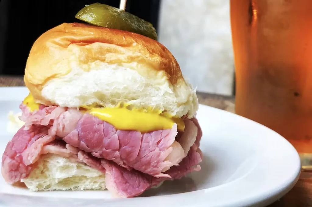 Close-up of a pastrami slider with mustard and a pickle spear.