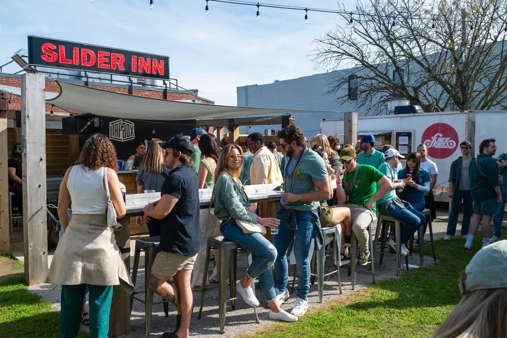Bustling Slider Inn outdoor patio with people in green under sunny sky.