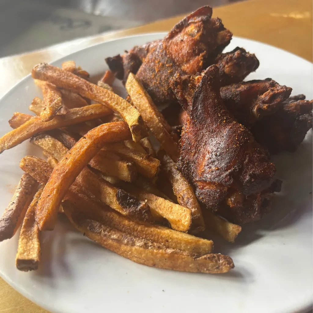 Close-up of a plate with seasoned chicken wings and crispy french fries.