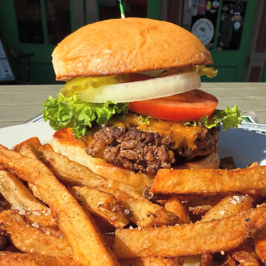 Close-up of a burger with cheese, fresh toppings, and seasoned french fries.