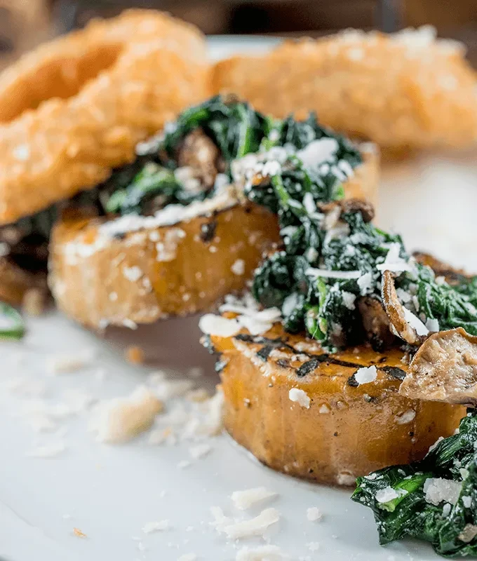 Charred root vegetable slices with sautéed greens, mushrooms, and cheese.