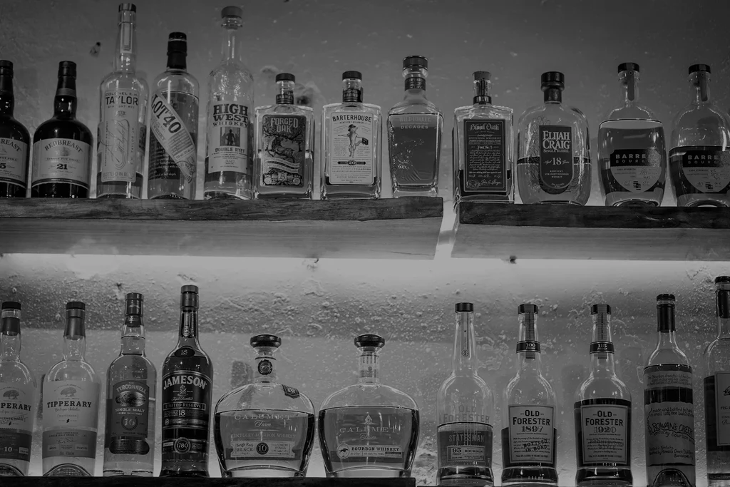 Black and white photo of two shelves with assorted whiskey and bourbon.