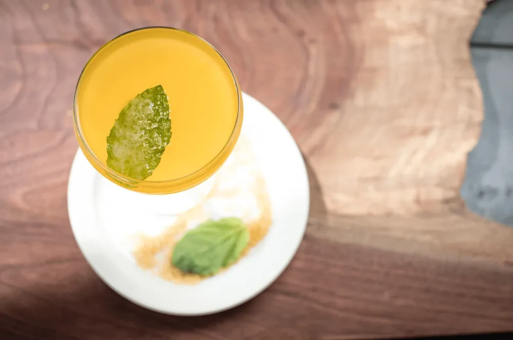 Top-down yellow cocktail with sugared mint on wooden table.