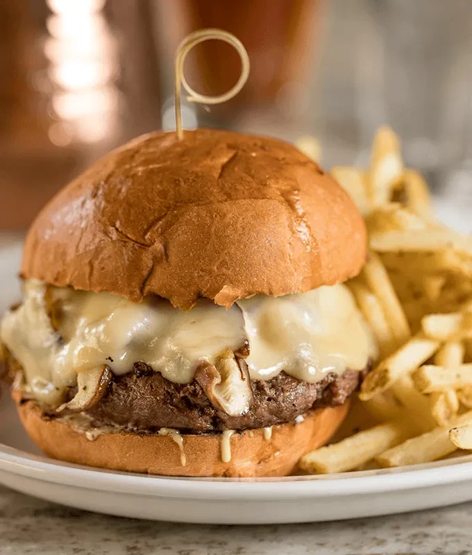 Gourmet burger with melted white cheese, fries, wooden skewer.