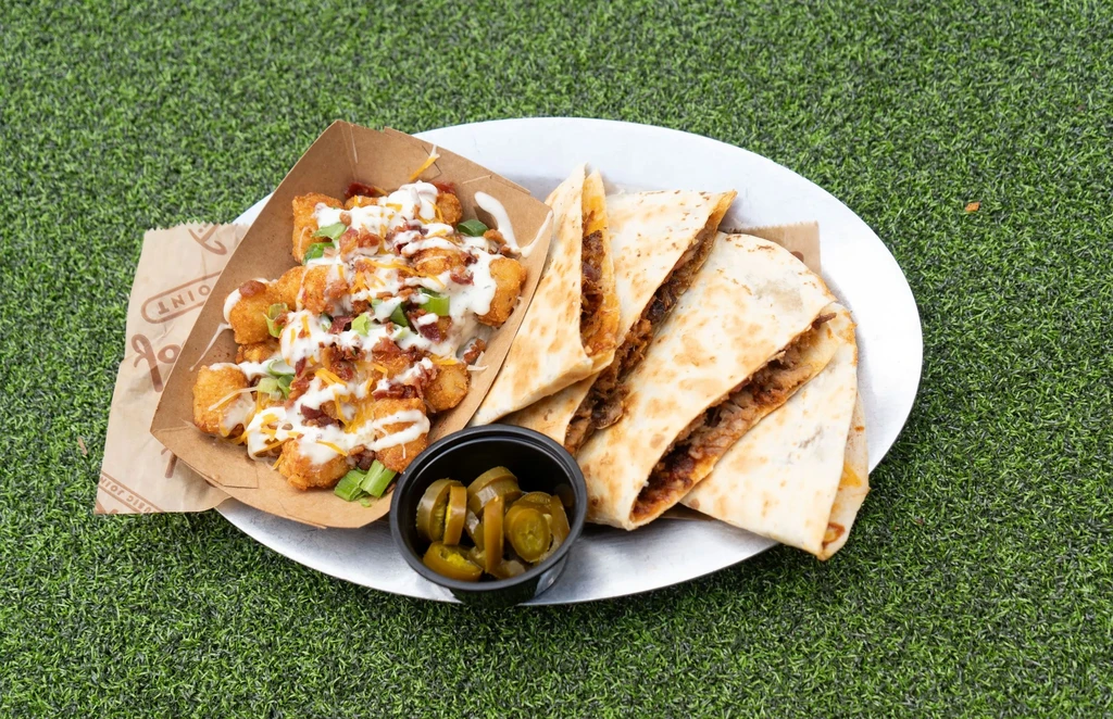 Close-up of loaded tater tots, quesadilla slices, and jalapeños on a tray.