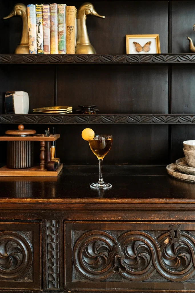 Amber cocktail with citrus peel on ornate antique cabinet.