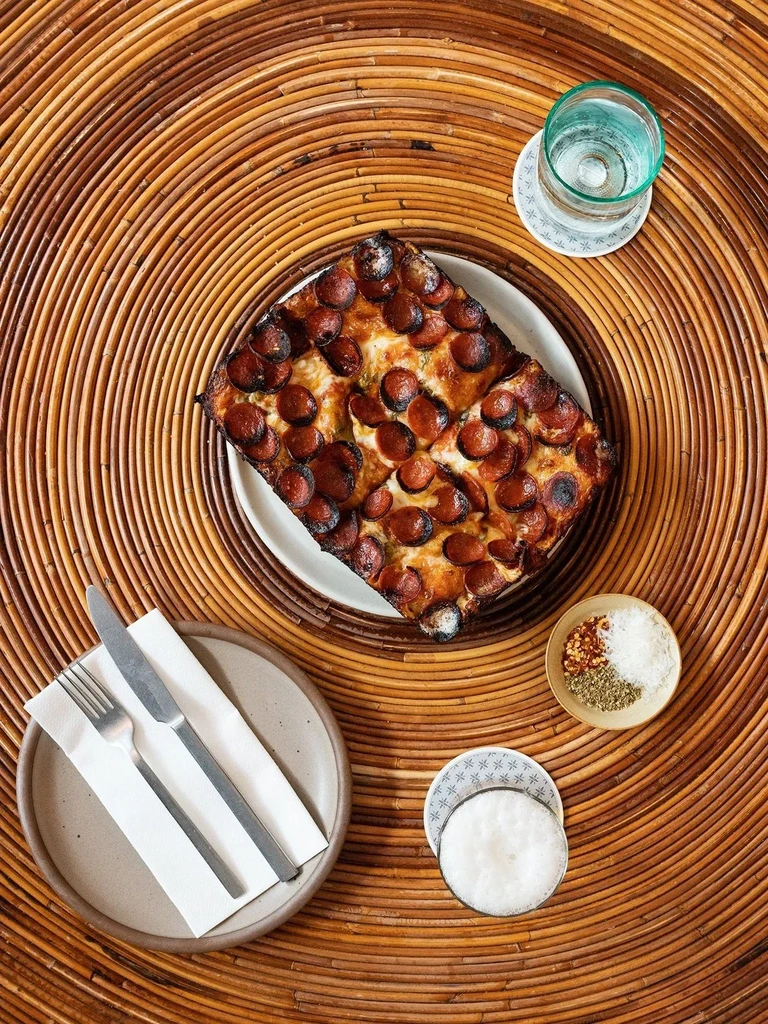 Overhead shot of deep-dish pepperoni pizza on a woven rattan table.