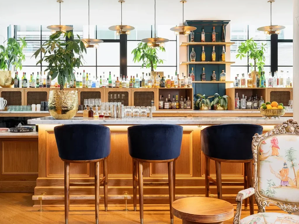 Bar area with marble counter, liquor bottles, plants, and velvet stools.