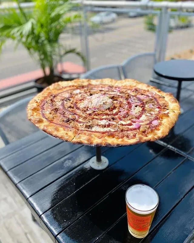Pizza with meat, red onions, and beer on an outdoor table.