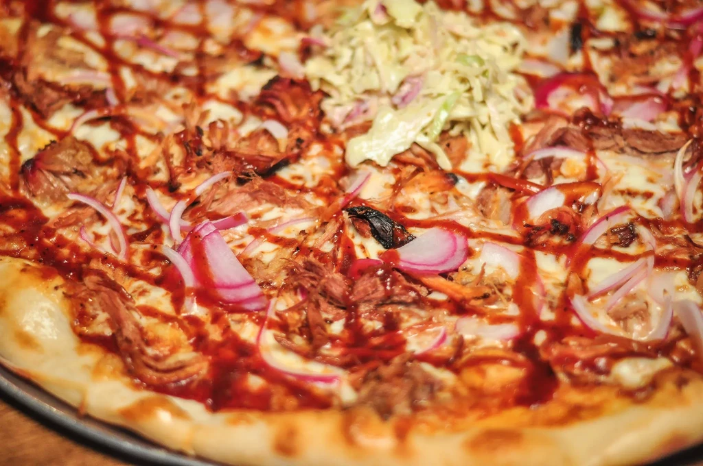 Barbecue pizza topped with shredded meat, cheese, red onion, and coleslaw.