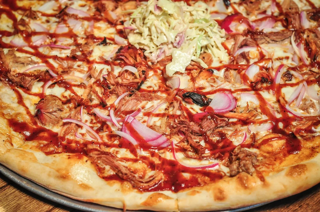 Pizza with pulled pork, BBQ sauce, red onion, and coleslaw.