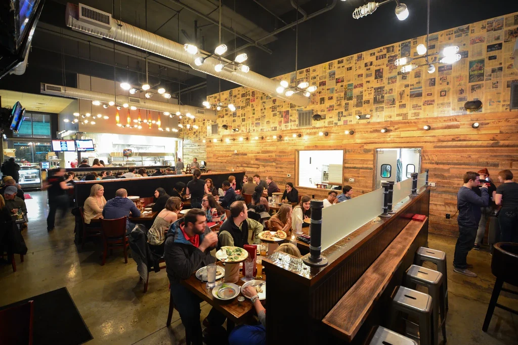 Bustling industrial-chic restaurant interior with many diners and staff.