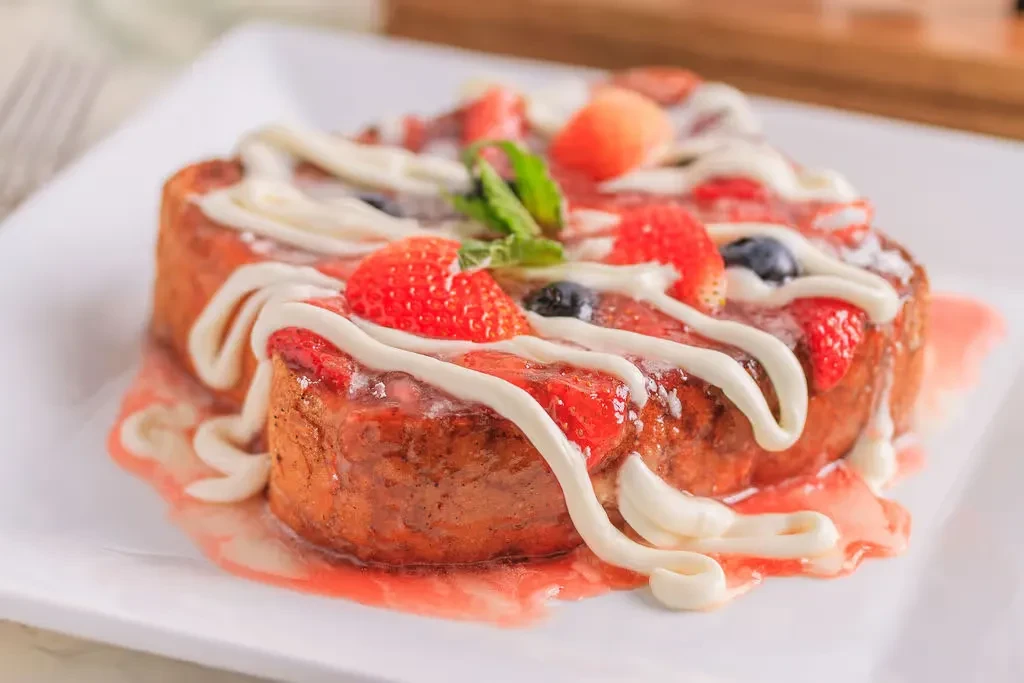 Golden French toast with fresh berries, mint, white drizzles, and syrup.