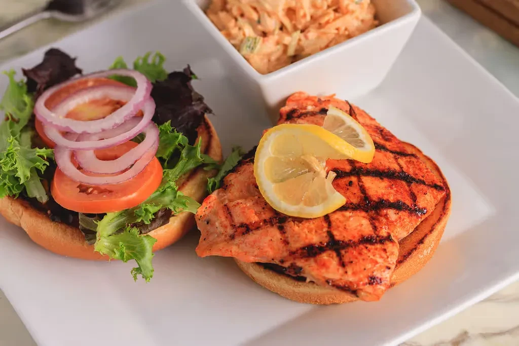 Deconstructed grilled fish sandwich with vegetables, lemon, and a side.