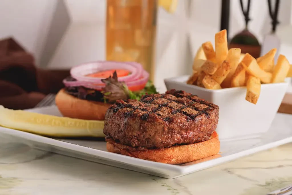 Grilled burger, golden fries, and pickle spear on a white plate.