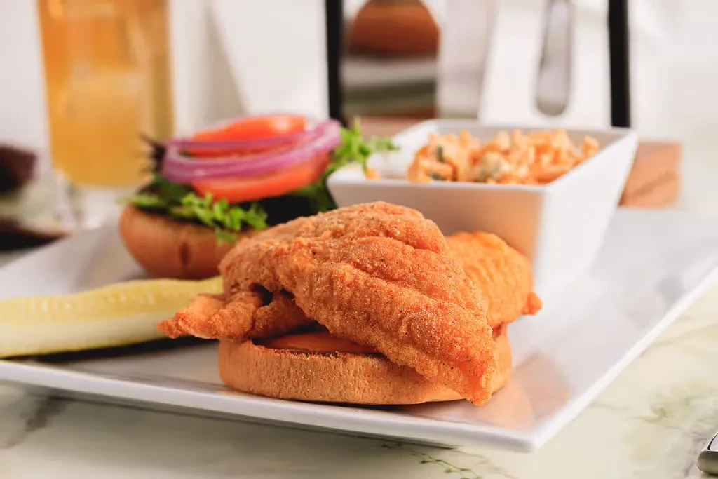 Crispy fried fish sandwich with pickle, coleslaw, and a drink.
