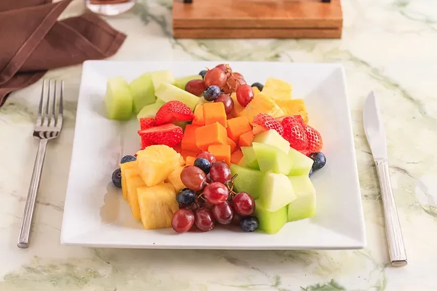 Assorted fresh cut fruit platter, fork, and knife on a table.
