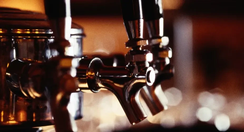 Close-up of several metallic beer taps in a dimly lit bar.
