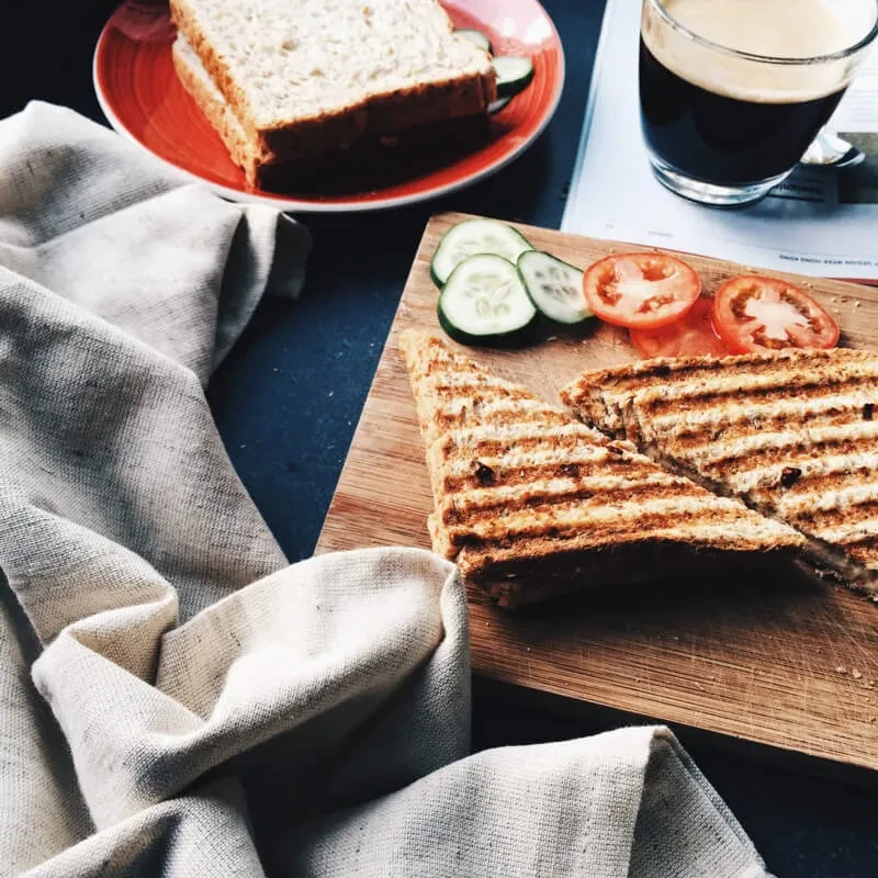 Overhead view of two sandwiches, coffee, and magazine on a dark table.