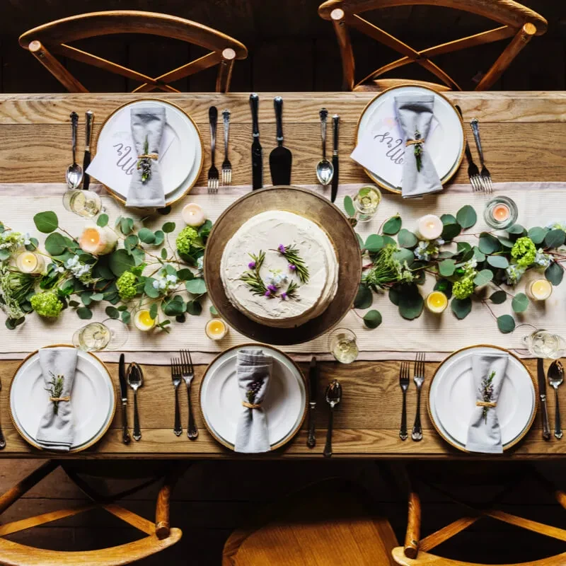Rustic table set with cake, candles, foliage, and 'Mr.' 'Mrs.' cards.