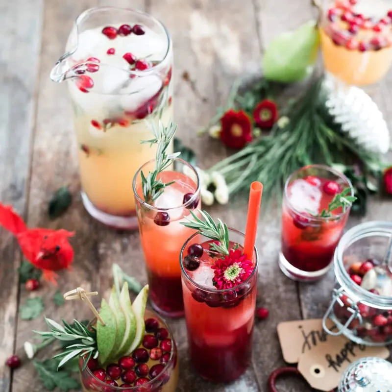 Colorful cocktails, a pitcher, and festive garnishes on wood.