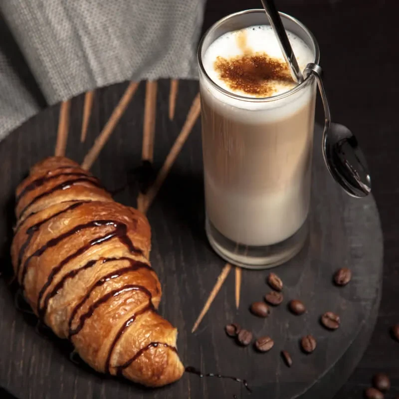 Chocolate-drizzled croissant and layered coffee on a rustic board.