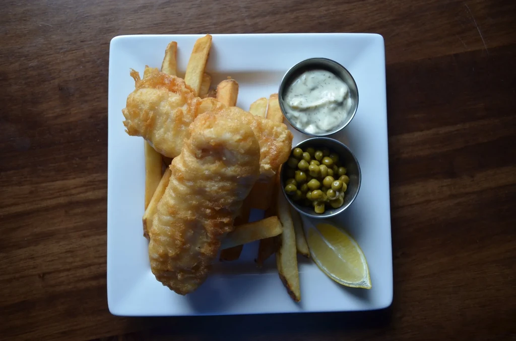 Golden-fried fish and chips, tartar sauce, peas, and lemon wedge.