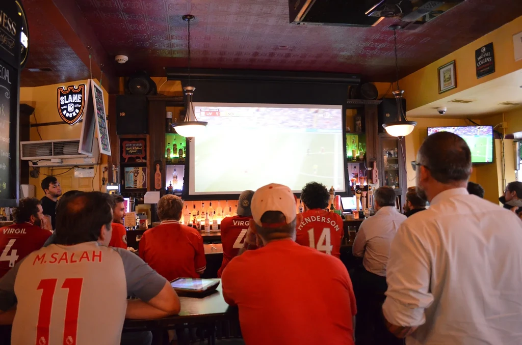 Patrons in jerseys watch a soccer game in a lively sports bar.
