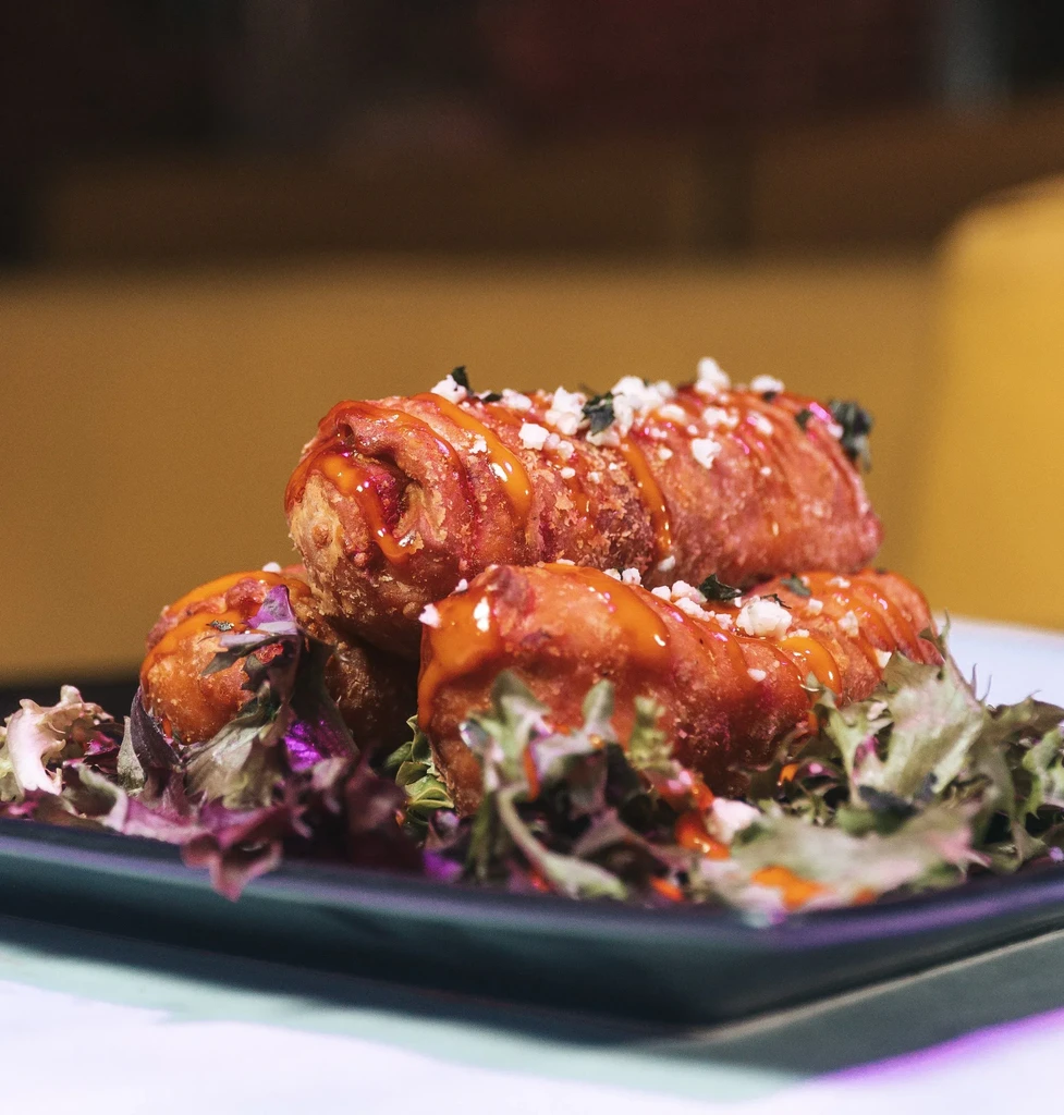Three golden fried items with orange sauce, cheese, herbs on greens.