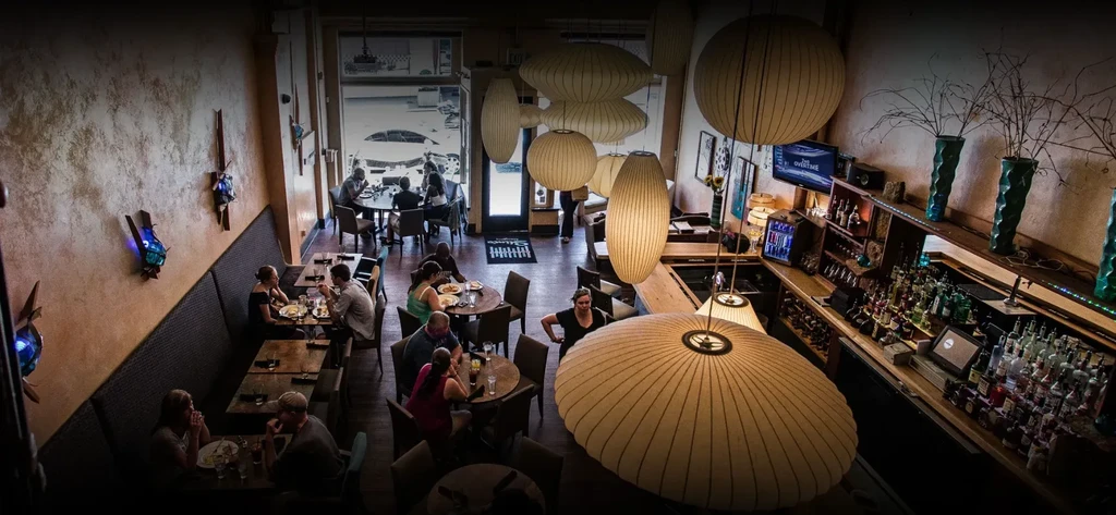 Aerial view of a warm restaurant interior with long bar and ceiling lanterns.