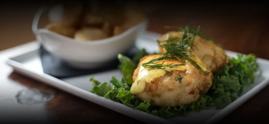 Two golden-brown crab cakes with creamy sauce, dill, and lettuce.