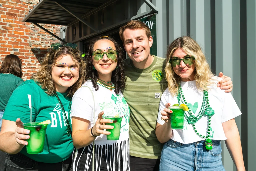 Four young adults in green celebrating St. Patrick's Day with drinks.