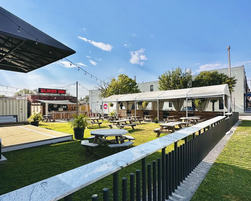 Sunny, grassy outdoor dining area with picnic tables and Slider Inn.