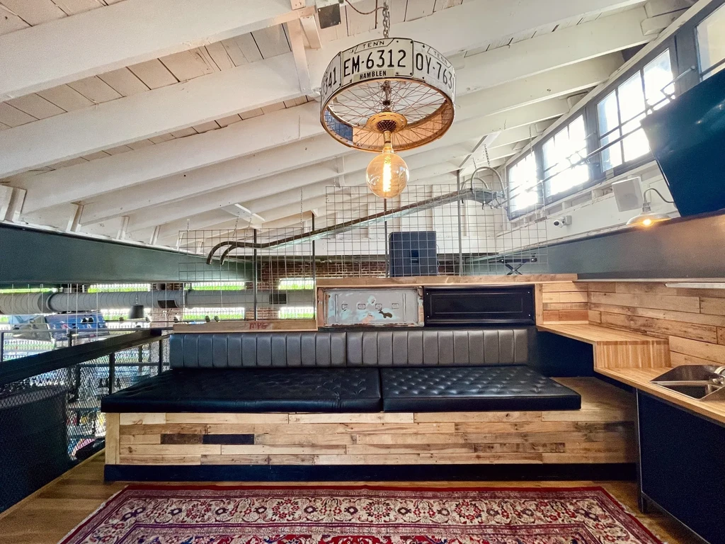Industrial-rustic mezzanine with tufted bench, oriental rug, license plate chandelier.