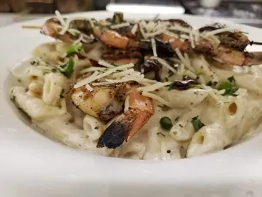 Creamy penne pasta with grilled shrimp, grated cheese, and green herbs.