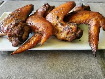 Four roasted chicken wings with crispy, seasoned skin on a white plate.