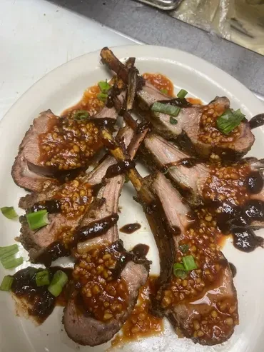 Grilled lamb chops with orange-red sauce, dark drizzle, and green onions.