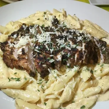 Creamy penne pasta topped with grilled chicken, cheese, and herbs.