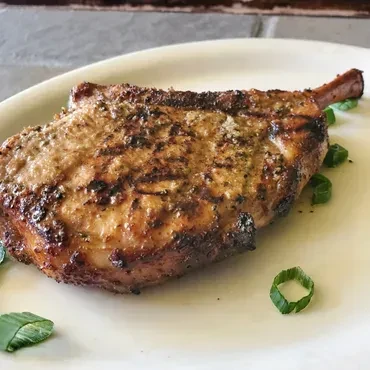 Golden-brown grilled pork chop with herbs and chives on a white plate.
