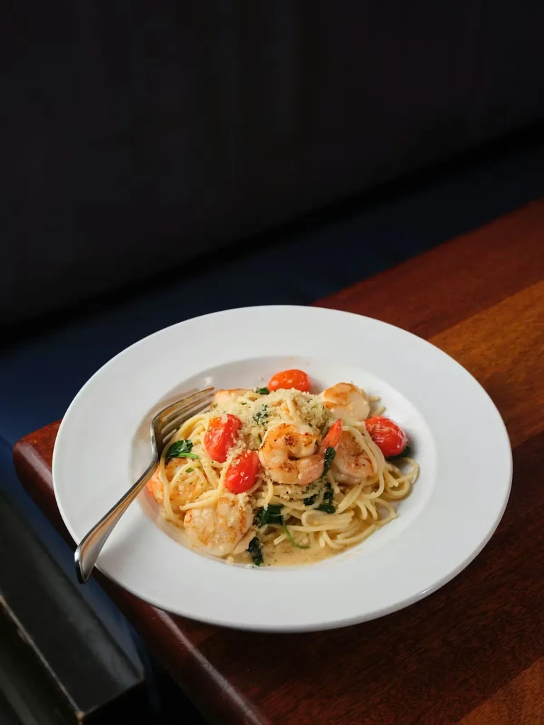 Close-up of creamy pasta with shrimp, scallops, tomatoes, cheese, and herbs.