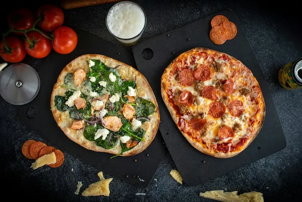 Two well-lit artisanal pizzas, white and red, with fresh ingredients.