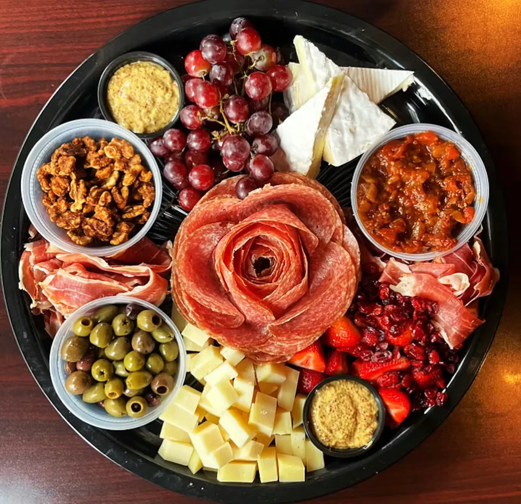 Circular charcuterie board with a salami rose, cheeses, meats, fruits, and olives.