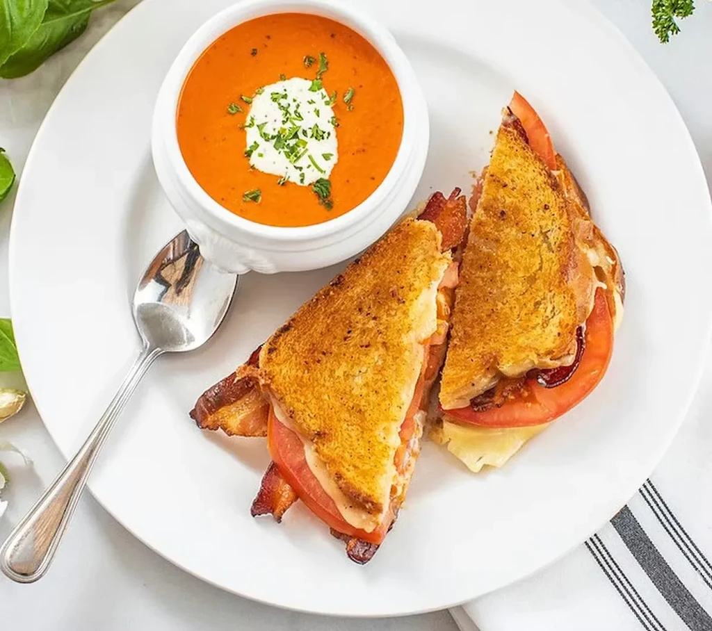 Bowl of tomato soup and grilled cheese with bacon and tomato.