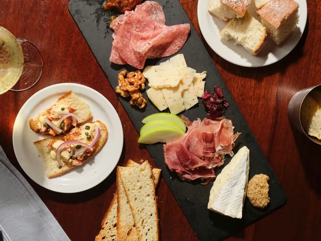 Dark slate charcuterie board, breads, and an appetizer on a wooden table.