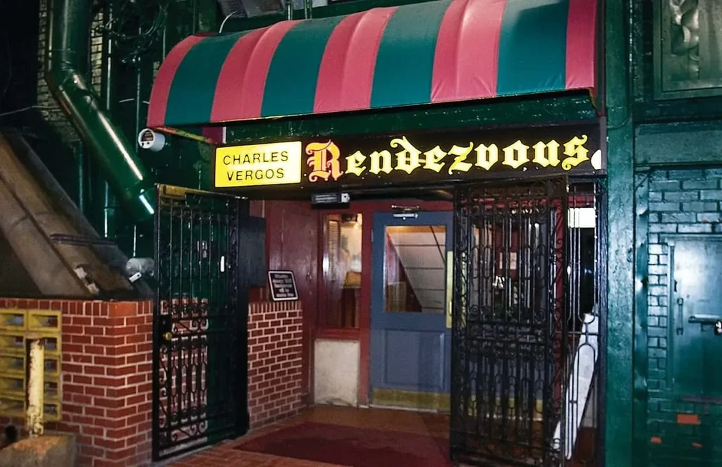 Nighttime CHARLES VERGOS Rendezvous entrance, striped awning, illuminated sign, ornate gates.