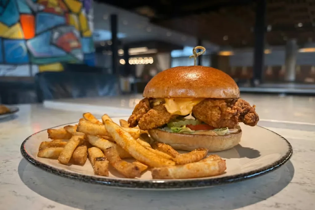 Gourmet fried chicken sandwich with melted cheese, lettuce, and seasoned french fries.