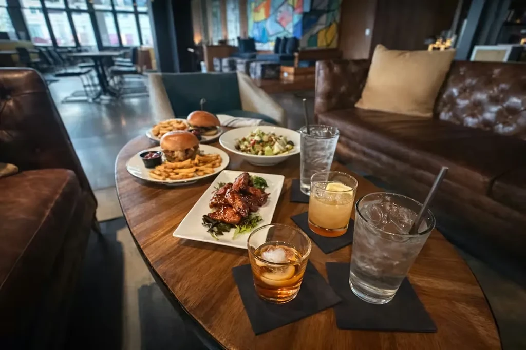 Restaurant table with burgers, fries, chicken wings, salad, and cocktails.