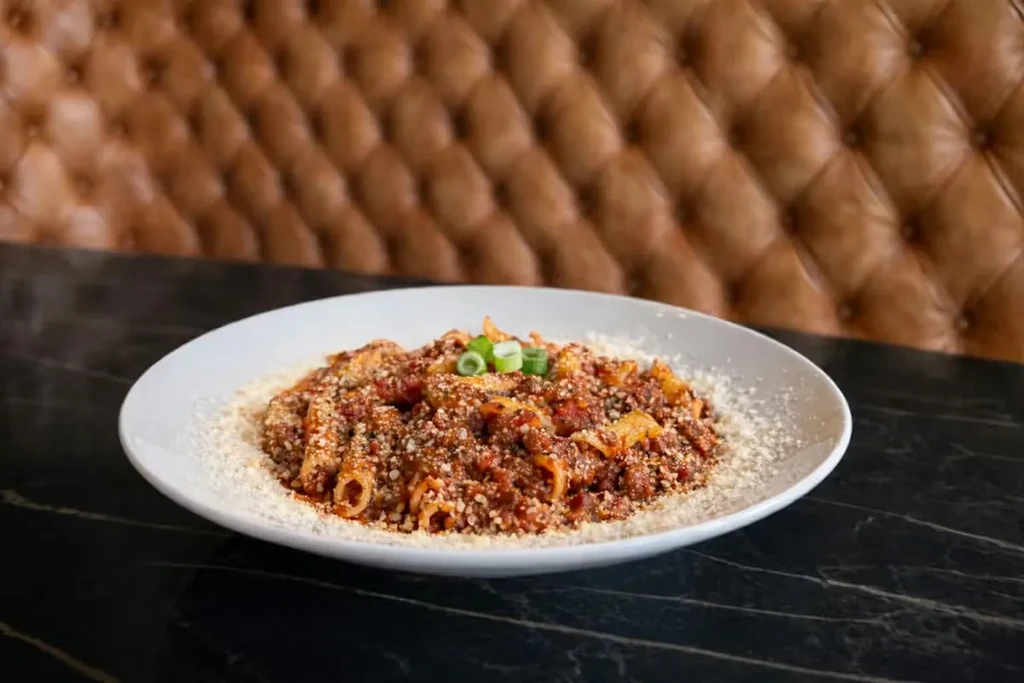 Plate of tube pasta with meat sauce, Parmesan, and green onion garnish.