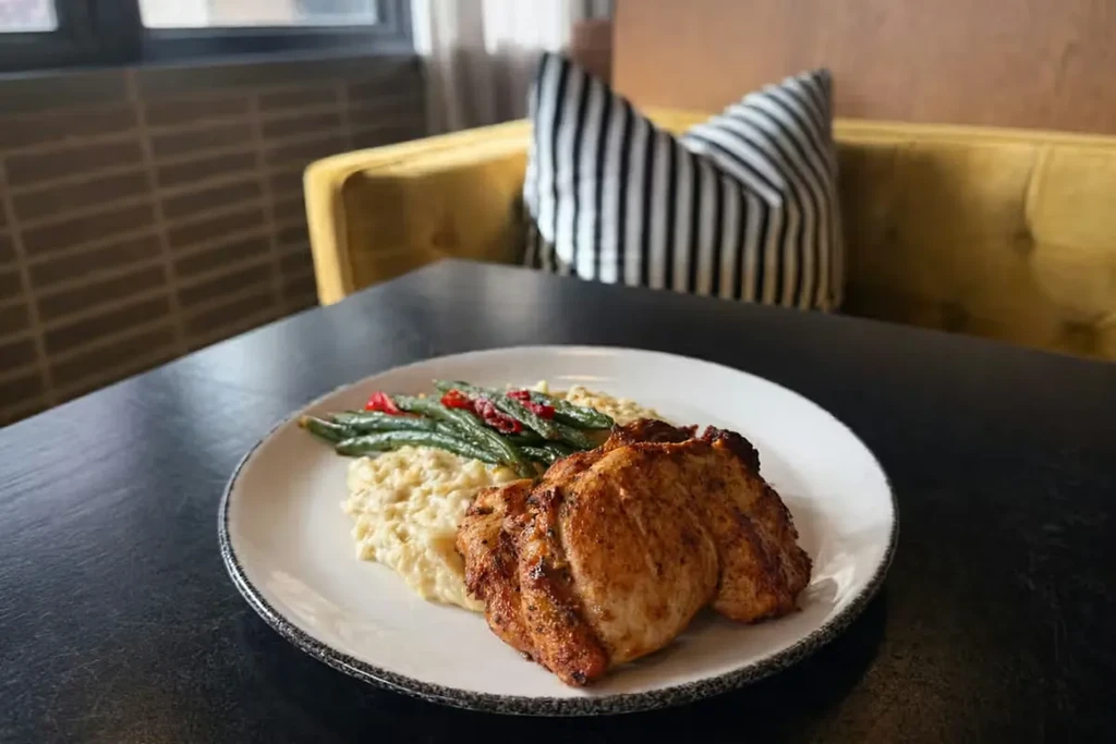 Close-up of plated chicken, creamy risotto, green beans, and peppers.