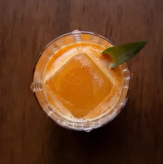 Vibrant orange cocktail with square ice and a green leaf garnish.